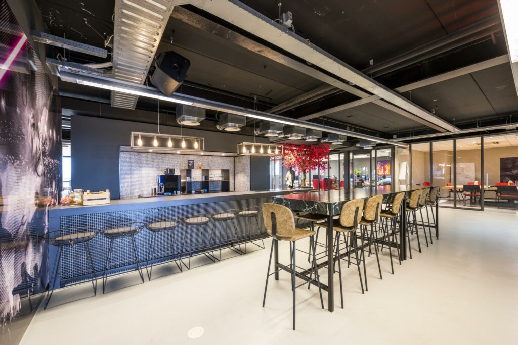 Moderne bedrijfskeuken en kantine aan de Anthony Fokkerweg met hoge tafels, barkrukken en een opvallende rode boomdecoratie.